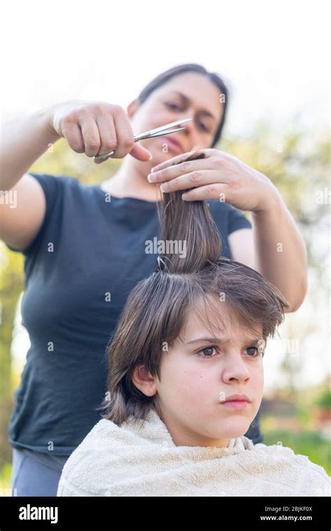 mother cuts her son s hair in the garden at home the mother is a hairdresser for her son stock