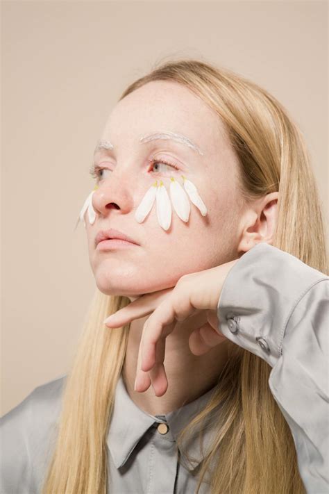 Serious young blondie with chamomile petals on face looking away in ...