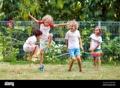 Happy Kids Play Outdoor Children Skipping Rope In Sunny Garden Summer