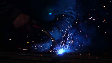 The Welder Works In A Mask In Slow Motion Sparks Fly In Different Directions Blue Color Glow