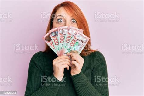 Beautiful Redhead Woman Holding 100 New Zealand Dollars Banknote Afraid