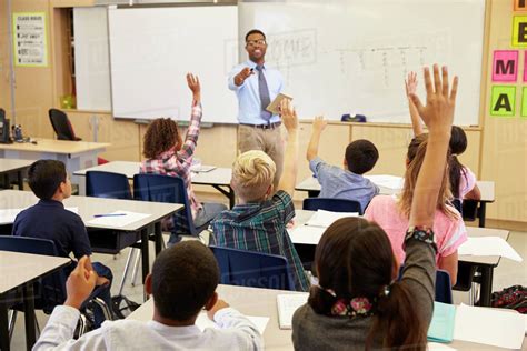 Kids Raising Hands To Answer In An Elementary School Class Stock