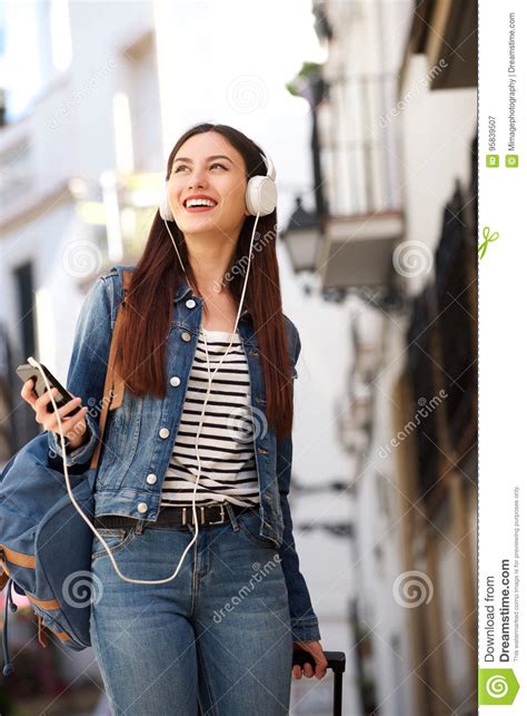 Happy Woman Walking With Headphones And Luggage Outside Stock Image