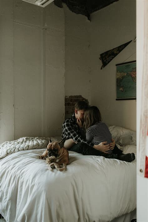 Couple Cuddling On Bed In Bedroom Next To Dog By Rachel Gulotta