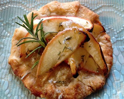 An Apple Pie With Rosemary Garnish On Top Sits On A Blue Tablecloth