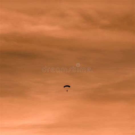 Silhouette Of Parachutist Flying Slowly On Parachute At Sunset Stock