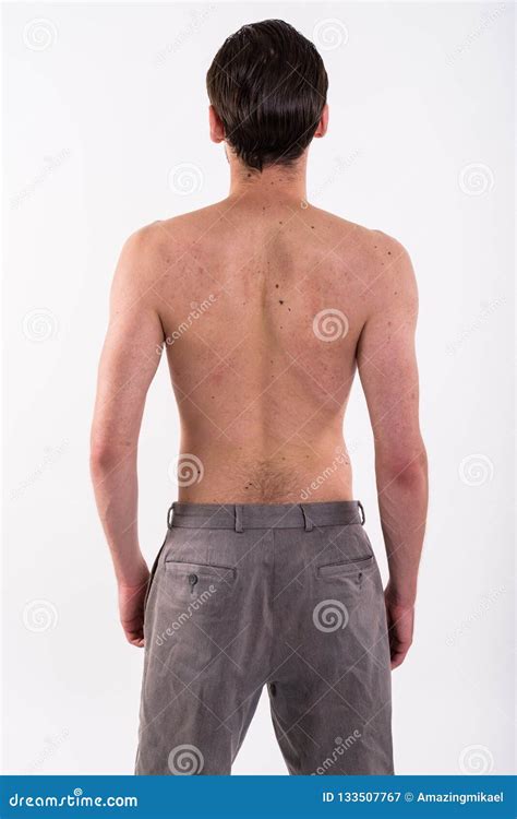 Studio Shot Of Back View Of Young Man Standing Shirtless Against Stock