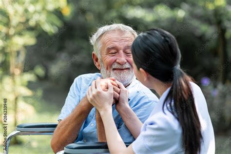 Caring Nurse With Senior Man Sitting On Wheelchair In Gaden Asian