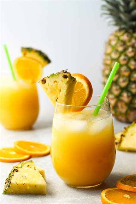 Two Glasses Filled With Orange Juice And Garnished With Pineapple