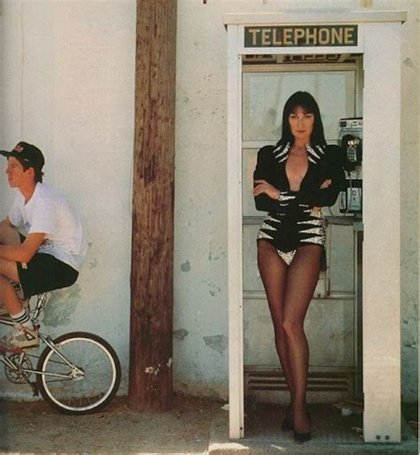 A Man Riding A Bike Next To A Woman Standing In Front Of A Telephone Booth