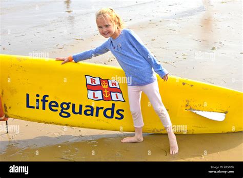 Six Year Old Girl Posing At Seaside Beside A Rnli Lifeguards Surfboard Awareness Idea Of Sea