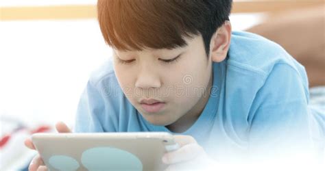 Asian Boy Lying And Playing Game On Digital Tablet At Home Stock Image