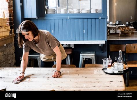 A Female Waitress Clearing A Table And Wiping It In A Cafe Stock Photo