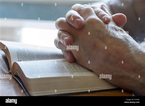 Weathered Old Mans Hands Clasped In Prayer Over Open Bible Stock Photo