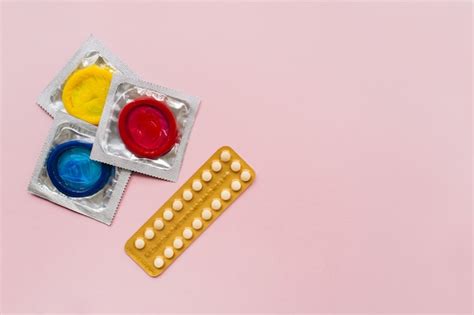 premium photo composition with colorful condoms and birth control pills on pastel pink