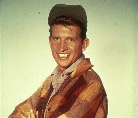 A Man Wearing A Plaid Jacket And Cap Smiles At The Camera With His Arms
