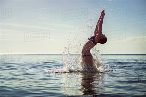 Seductive Woman Splashing Water While Diving Into Sea Against Sky
