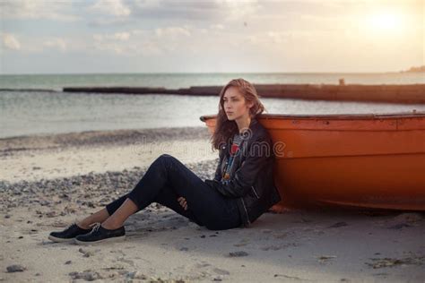 A Girl Sideways Near A Red Boat On The Beach By The Sea Stock Photo