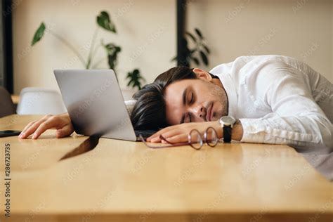 Young Tired Man With Laptop Sleeping On Desk At Work In Office Stock