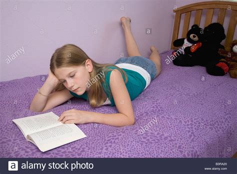 Young Girl Lying On Bed On Her Stomach Reading A Book
