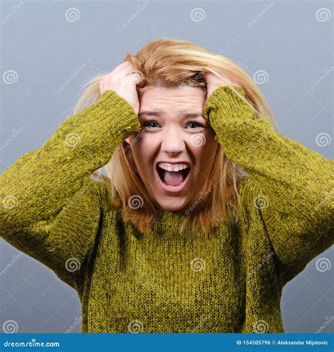 Portrait Of A Hysterical Woman Pulling Hair Out Against Gray Background