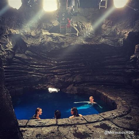 Three People Sitting In A Cave With Blue Water And Sunlight Coming