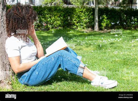 Curly Haired Girl Sitting On The Grass And Leaning Against A Tree While
