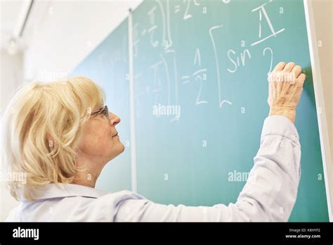 Senior Woman As Math University Teacher Writes On Chalkboard Stock