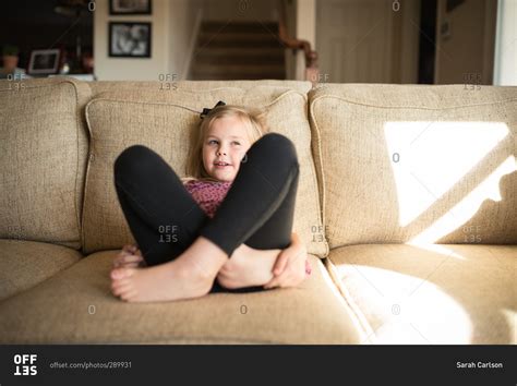Little Girl Sitting On A Couch With Her Legs Crossed And Knees Up Stock