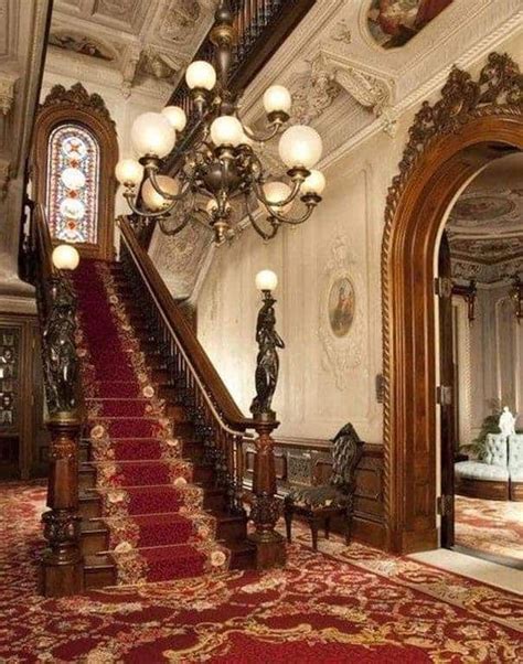 An Ornate Staircase With Chandelier And Red Carpeted Area In Front Of It