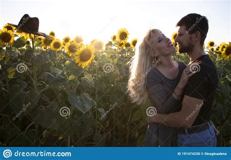 Beautiful Young Couple Kissing In A Field Of Sunflowers At Sunset A Blonde In A Black Hat And A