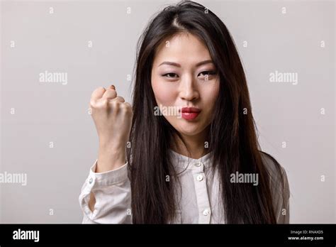Portrait Of Asian Woman In White Shirt Showing Fist On Gray Background