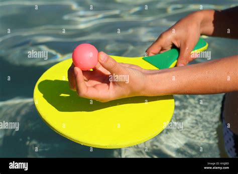 A Hand Holds A Ball And A Racket In The Water To Play Paddle Beach
