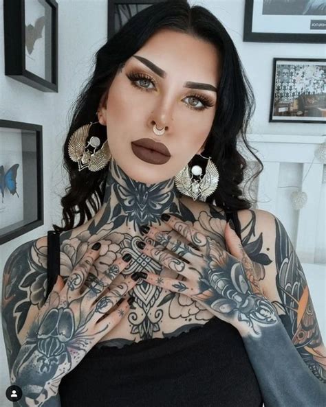 a woman with tattoos and piercings on her chest posing for a photo in front of some pictures