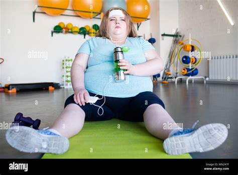 full length portrait of tired obese woman sitting on yoga mat on floor and listening to music