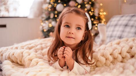 Cute Little Girl Is Lying Down On Bed In Bokeh Christmas Tree