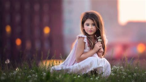 Cute Baby Girl Is Sitting On Green Grass Having Flowers In