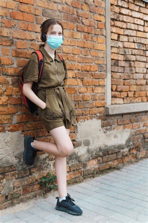 Schoolgirl Poses Against A Brick Wall In The Backyard Of The School Wearing A Protective Mask