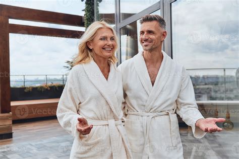 Beautiful Mature Couple In Bathrobes Enjoying Fruits And Wine While Relaxing In Luxury Hotel