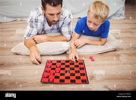 Father And Son Playing Checker Game While Lying On Hardwood Floor Stock