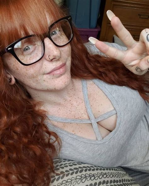 A Woman With Red Hair And Glasses Making The Peace Sign