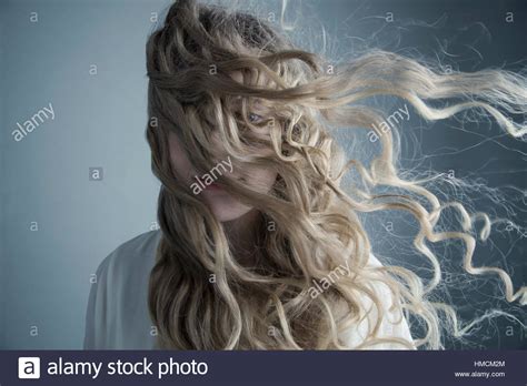 Portrait wind blowing long curly blonde hair across face ...
