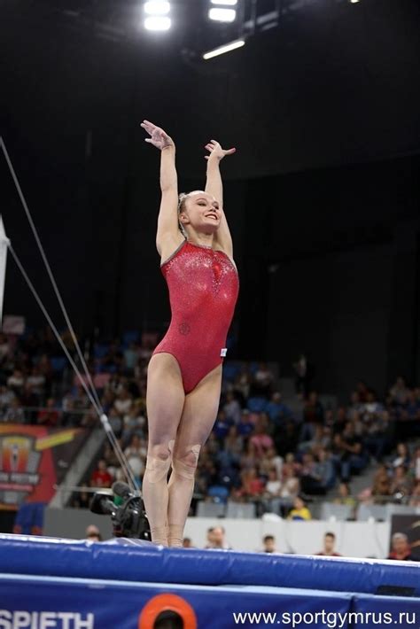 A Woman In A Red Leotard Standing On A Balance Beam With Her Arms Up