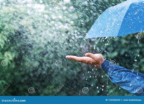 Hand And Blue Umbrella Under Heavy Rain Against Nature Background