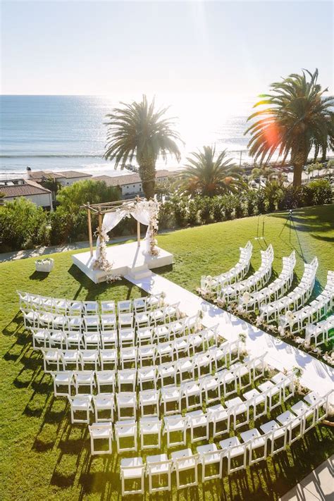 An Outdoor Ceremony Setup With White Chairs And Palm Trees On The Lawn