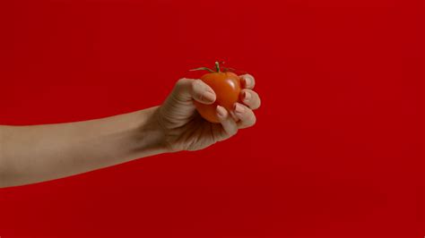 Wide View Of Woman Hand Squeezing Juice From Tomato On Red Background