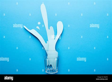 Top View Of Glass With Paper Cut Water Splash On Blue Background Stock