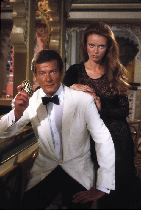 A Man In A White Tuxedo Holding A Cell Phone Next To A Woman