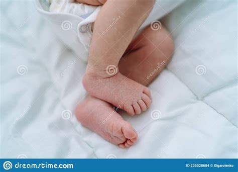 Close Bare Feet Of Newborn Unrecognizable Child In White Clothes On