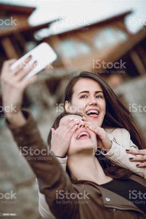 Cute Girl Taking Selfie While Her Friend Surprise Closed Her Eyes Stock